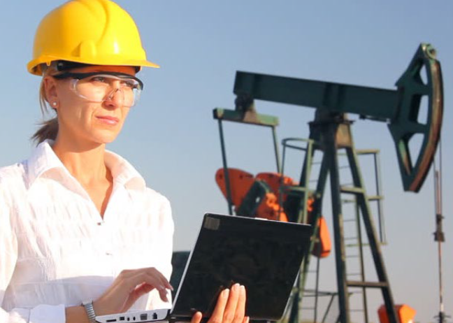 Woman in hardhat with computer near pumpjack